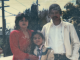 A Latina mom wearing a red suit dress, a young girl, and her father stand in a photo outdoors